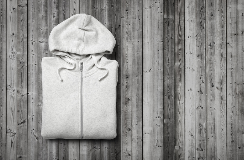 A neatly folded light grey hoodie with a full front zipper and an attached hood with drawstrings, placed flat on a weathered wooden surface with vertical planks, displaying natural knots and grain patterns. The hoodie appears to be made of soft, cotton-blend fabric with a smooth, slightly textured finish, and its clean, simple design is free of logos or embellishments. The wooden surface provides a neutral, rustic background, emphasizing the garment's light colour and detail. The image depicts an indoor setting or outdoor surface, with natural lighting highlighting the fabric's texture and the wood’s aged appearance, consistent with a scene that might be taken during rubbish removal or decluttering at a property in London or nearby areas, where White Goods Recycle often operates. This detailed visual context supports environmentally responsible disposal or recycling of textile waste, aligning with waste management services specializing in sorting and recycling household items.